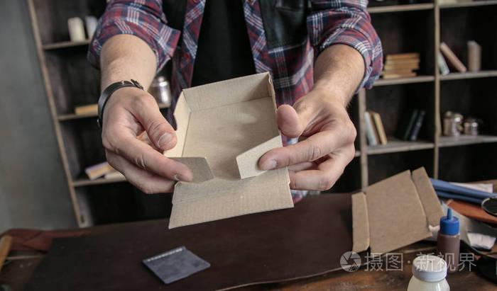 年轻男子皮革制造商手动组装产品的纸板包装盒子